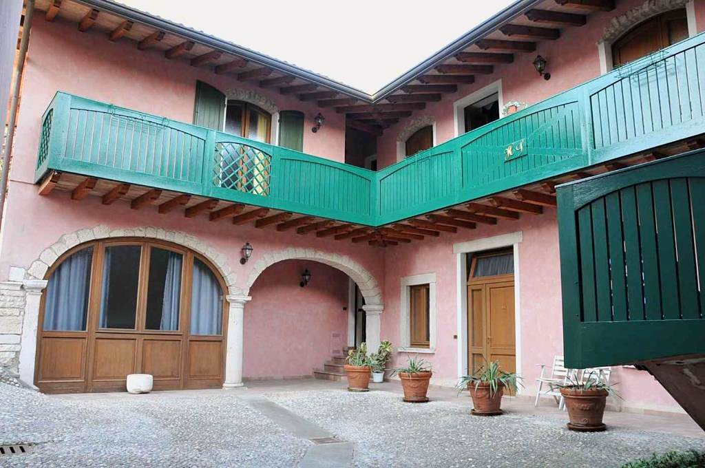 La corte interna dell'Hotel Sogno: casa rosa a due piani con ballatoio verde e archi in pietra